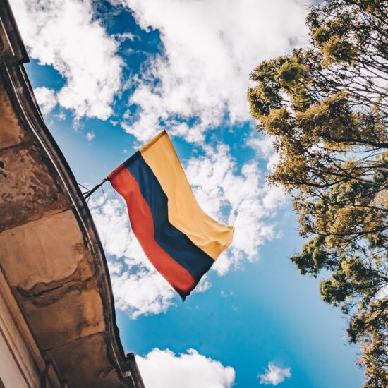 a Colombian flag with the sky, trees, and a building